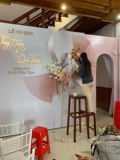 a woman standing on top of a wooden stool next to a wall covered in flowers