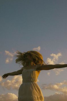 a woman in a white dress is flying a kite with her arms spread out to the sky