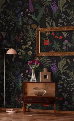 a vase with flowers sitting on top of a wooden table next to a framed painting