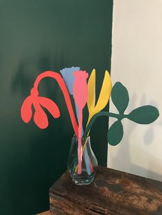 a vase filled with colorful paper flowers on top of a wooden table next to a green wall