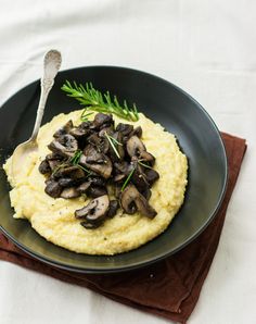 mashed potatoes topped with mushrooms and sprigs in a black bowl on a brown napkin