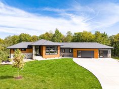 a large house with two garages in the middle of a grassy area next to trees