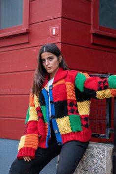 a woman leaning against a wall wearing a colorful sweater