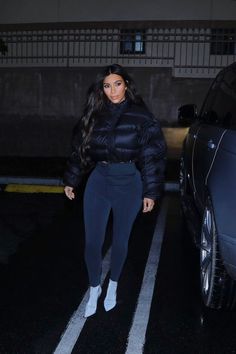 a woman in black jacket and leggings standing next to a car at night