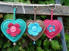 three crocheted hearts hanging from a clothesline with buttons and flowers on them