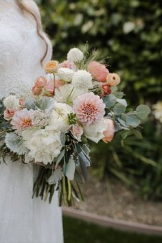 a bride holding a bouquet of white and pink flowers with greenery in the background