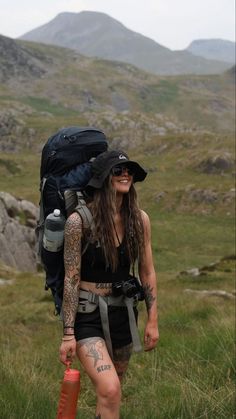 a woman with long hair and tattoos walking in the mountains carrying a backpack on her back