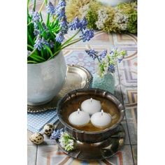 three white candles sitting on top of a table next to a vase filled with flowers