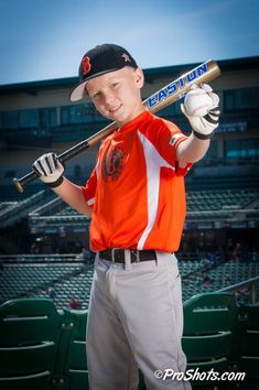 a young baseball player is posing with his bat and ball in the other hand while wearing an orange shirt