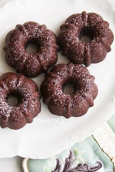 three chocolate donuts are on a white plate