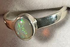 "This beautiful Opal ring is handmade and weighs 3 grams. The band of the ring is made of sterling silver. The oval is round in shape and displays a play of colours. These colours include red and green. Size \"R\"" Multicolor Oval Ruby Ring For Gift, Multicolor Oval Ruby Ring Gift, Oval Multicolor Hallmarked Ring, Multicolor Oval Hallmarked Ring, Formal Multicolor Opal Ring, Multicolor Oval Opal Ring For Formal Occasions, Adjustable Green Oval Opal Ring, Adjustable Emerald Ring For Formal Occasions, Formal Adjustable Emerald Ring