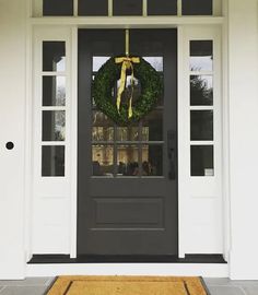 a black front door with a wreath and yellow ribbon hanging on it's side