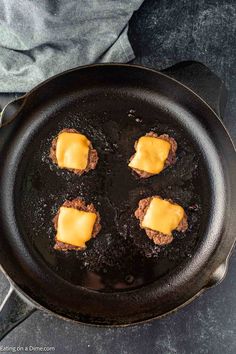 four hamburger patties cooking in a cast iron skillet with cheese on the top