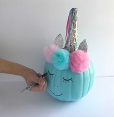 a person is painting a blue pumpkin with unicorn ears and pompoms on it