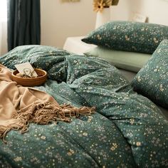 an unmade bed with green comforter and pillows on it, next to a basket full of flowers