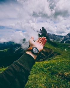 a person's hand reaching up into the sky with mountains and clouds in the background