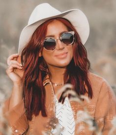 a woman with red hair wearing sunglasses and a white hat is posing for the camera