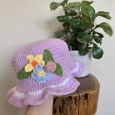 a purple crocheted hat with flowers on it sitting next to a potted plant