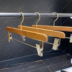 three wooden clothes hangers on a metal rail in a public restroom with black tile flooring