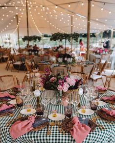 an outdoor tent with tables and chairs covered in plaid cloths, pink napkins and place settings