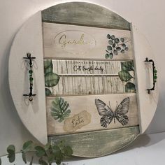 a white wooden plaque with butterflies and leaves on it, hanging from the wall next to a potted plant