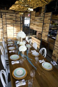 a dining room table set with white and gold plates, silverware, and flower centerpieces