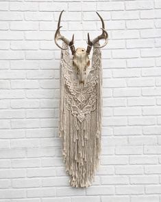 an animal skull with long horns and fringes hanging on a brick wall next to a white brick wall