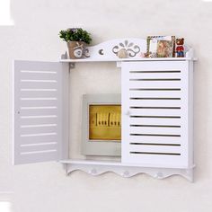 a white wall mounted shelf with an electronic device on it's side and flowers in the corner