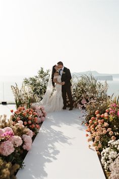 a bride and groom kissing in front of flowers at their wedding ceremony by the ocean