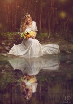 a woman in a white dress sitting on top of a body of water holding flowers