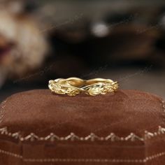 a gold wedding band sitting on top of a brown velvet hat box with other jewelry items in the background