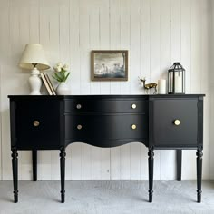 a black dresser with three drawers and two lamps on top of it in front of a white wall