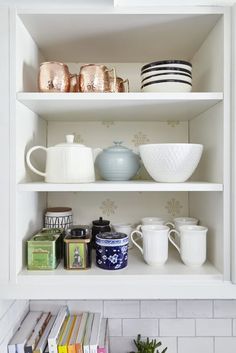 the shelves in the kitchen are filled with dishes and mugs on top of them