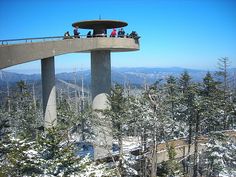 people standing on top of a tall tower in the middle of trees and snow covered ground