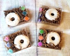 three donuts are sitting in small boxes on the table with buttons and glue paint