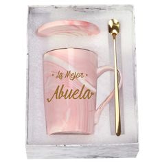 a pink marble coffee mug and spoon with the words be merry abuela written on it