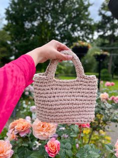 a hand holding a straw bag in front of pink flowers