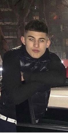 a young man wearing a black leather jacket posing for a photo in front of a car