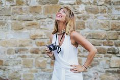 a woman standing in front of a brick wall holding a camera