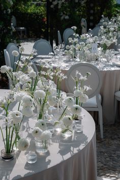 white flowers are in vases on the table at an outdoor wedding reception with chairs and tables