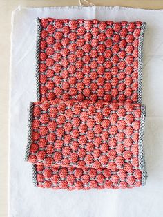 two crocheted red and gray squares on white fabric, one is folded in half