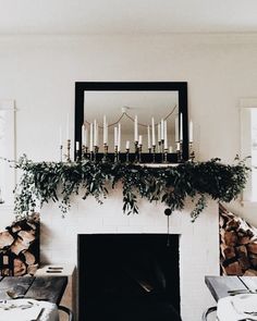 the fireplace is decorated with greenery and candles in front of an empty dining table