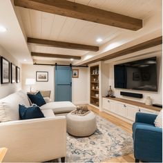 Modern basement living room with a white sectional sofa, blue accents, a wall-mounted TV, and exposed wooden ceiling beams. Cottage Basement, Basement Designs, Basement Fireplace