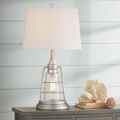 a lamp on top of a table next to a book and some seashells