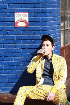 a man sitting on top of a bench drinking from a cup in front of a blue wall