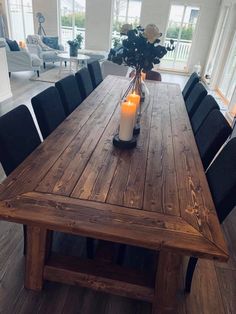 a wooden table with black chairs and a candle on it in front of a large window