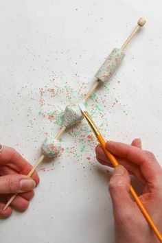 two hands holding toothbrushes over a paper with sprinkles on it