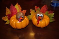 two fake turkeys sitting on top of pumpkins with leaves in front of them