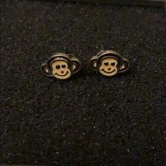 pair of monkey face stud earrings on black carpeted surface with white border around them