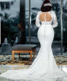 a woman in a white wedding dress looking at the back of her gown, which is open